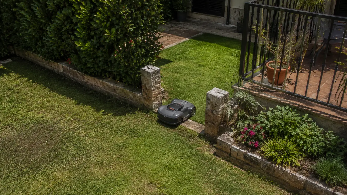 Robot cortacésped compacto cruzando un paso estrecho en un jardín pequeño