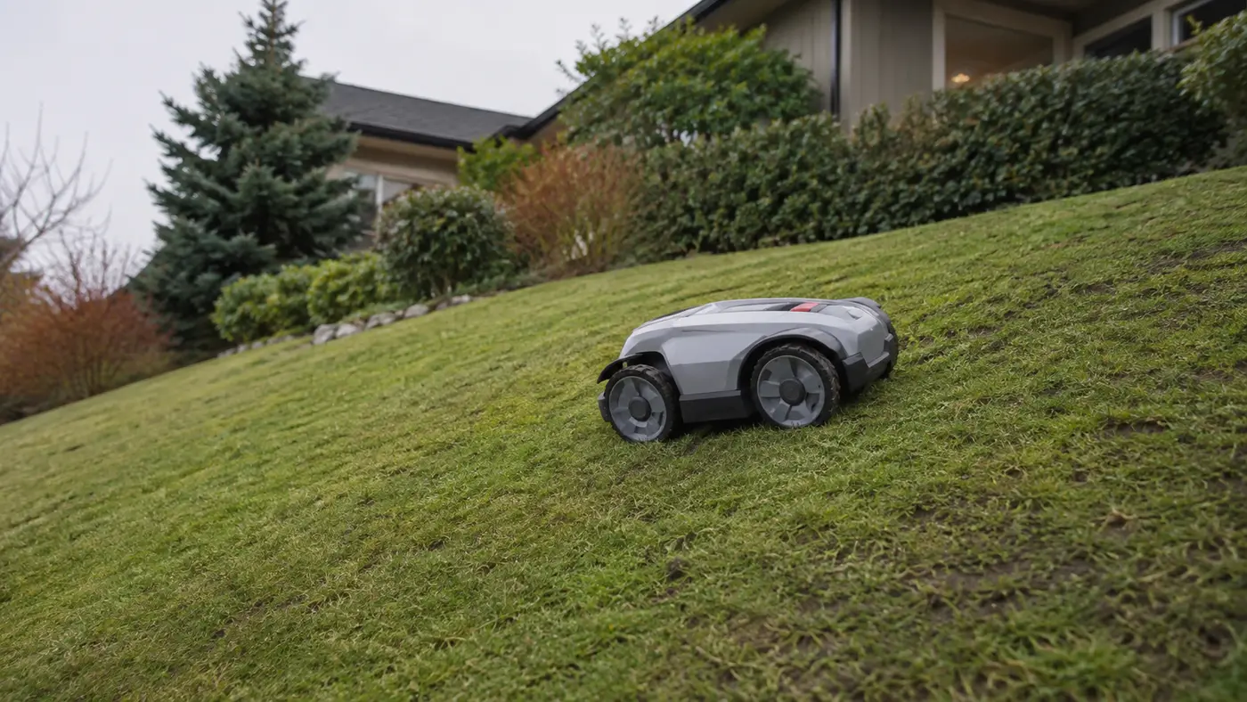 Robot cortacésped de tracción total recorriendo una pendiente de césped residencial
